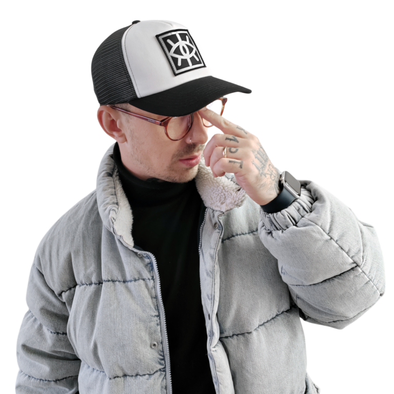 Hombre con gorra y chaqueta gris, ajustándose la gafas y mirando hacia un lado.